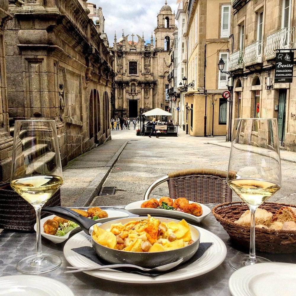 Terraza de Tixola Tapería en Rúa Juan de Austria con una tixola de raxo, croquetas y dos copas de vino blanco, y la iglesia de Santa Eufemia de Ourense al fondo